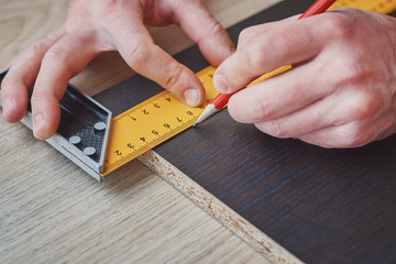 Wall Mural - carpenter hands taking measurement of wooden plank, closeup