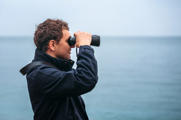 Young man looking into the distance through binoculars against the sea