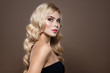 Elegant model portrai. Blonde haired Woman with blue eyes and Healthy Long Shiny Wavy hairtyle. Volume shampoo. Blond Curly permed Hair and bright makeup.  Beauty salon and haircare concept.