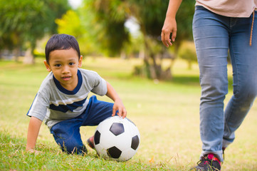 happy Asian Indonesian mother playing football with little 5 years old son running together excited laughing having fun in soccer fan child and healthy lifestyle education