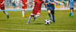 Leinwandbild Motiv Football Soccer Players Running with Ball. Footballers Kicking Football Match. Young Soccer Players Running After the Ball. Kids in Soccer Red and Blue Uniforms. Soccer Stadium in the Background