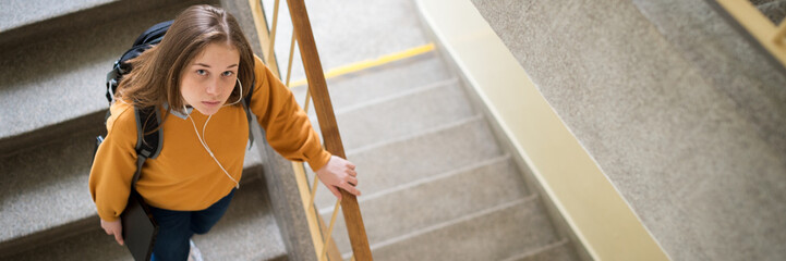 Young depressed lonely female college student walking down the stairs at her school, looking up at the camera. Education, Bullying, Depression concept.