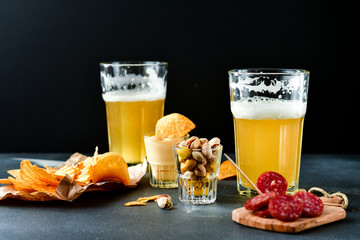 two glasses of beer and snacks chips, nachos with sauce, pistachios and salami, aperitif, relax in the bar with friends, beer party.  selective focus and copy space