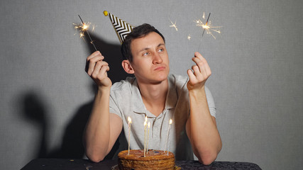 Wall Mural - Sad lonely man in party hat celebrating birthday alone and holding the sparkler.