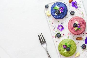 Wall Mural - matcha, blueberry, acai vegan cashew cakes with fresh berries, edible flowers, mint, nuts. healthy vegan food concept