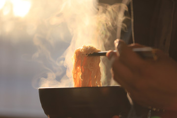 Man hand holding chopsticks of instant noodles in wood bowl with smoke rising in the home sunset background, Sodium diet high risk kidney failure, Healthy eating concept