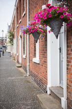 Beautiful City Town Houses With A Cobble Pebble Road And Beautiful Vibrant Pink Flowers In Hanging Baskets. Beautiful European Town Houses.shallow Depth Of Field.