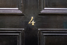 House Number 4 In Bronze As A Numeral On A Black Wooden Door