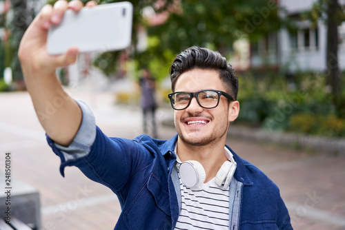 Fotografía Handsome student taking selfie with smartphone while outdoors on campus