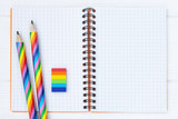 Fototapeta Tęcza - Open copybook with two rainbow-coloured pencils and a rubber on white wooden table