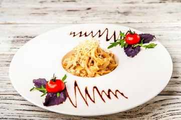 Fettuccine with chicken and mushrooms in a creamy sauce on a white plate. Traditional Italian pasta with sauce, tomatoes and basil close-up and copy space.