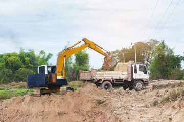 Wall Mural - Yellow excavator machine loading soil into a dump truck at construction site