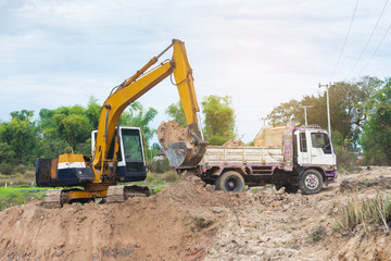 Wall Mural - Yellow excavator machine loading soil into a dump truck at construction site