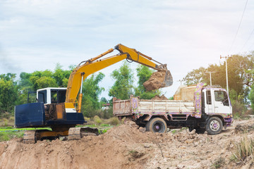 Wall Mural - Yellow excavator machine loading soil into a dump truck at construction site