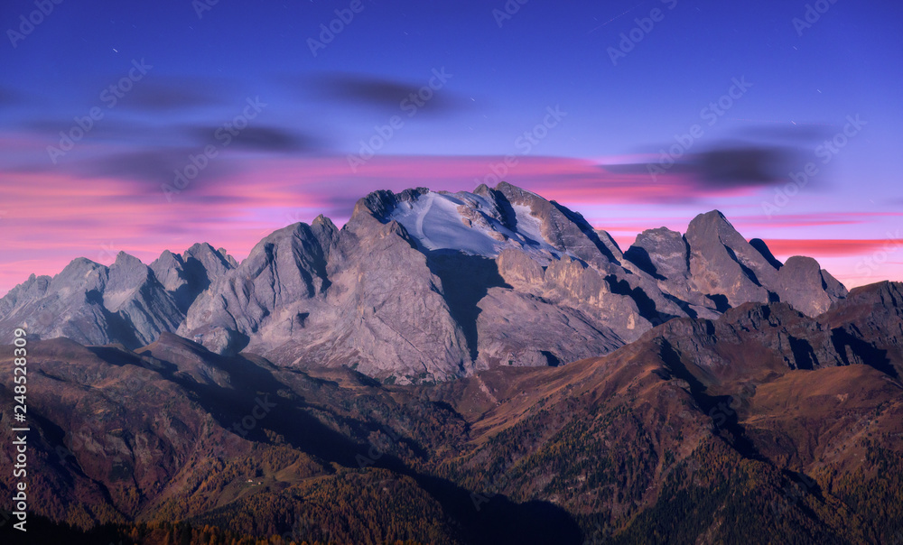Mountain peak lighted by moonlight in autumn at night in Dolomites, Italy. Beautiful landscape with mountains, forest on hills, purple sky with pink clouds, stars at dusk. Italian alps. High rocks  - obrazy, fototapety, plakaty 