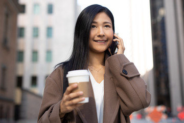 Canvas Print - Young Asian woman in city walking talking on cell phone