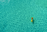 Fototapeta Nowy Jork - Aerial view of slim woman swimming on the swim mattress in the transparent turquoise sea in Seychelles. Summer seascape with girl, beautiful waves, colorful water. Top view from drone