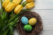 Easter background with bright, colored eggs in nest and yellow tulips. Top view with copy space.