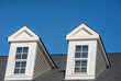 Double white dormer sash window with blue sky background on a gable roof with vinyl siding on a luxury estate house in the East Coast of the USA for upper middle class families