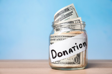 Glass jar with money and label DONATION on table against color background. Space for text