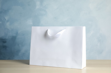 Wall Mural - Paper shopping bag on table against color background. Mock up for design