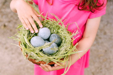  Beautiful cute baby girl is holding a basket with gray eggs on a Sunny summer day.Concept of family traditions.