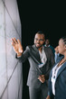 © JonoErasmus - Black african businessman pointing to large video screen for a presentation during a conference. To his female colleague and team