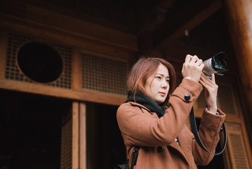 Wall Mural - Young woman traveler taking photo picture at jing'an temple in china. Young asian woman in jacket clothes using camera take a picture of temple in shanghai.