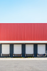 Front view of four truck loading docks at a warehouse in the suburbs of Paris, France, with white roller shutter doors closed under a red corrugated metal siding.