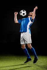 Wall Mural - handsome football player in uniform jumping with ball isolated on black