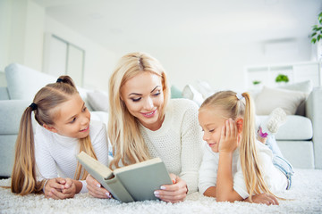 Sticker - Portrait of three nice-looking cute pretty lovely sweet attractive charming cheerful people pre-teen girls mom mommy lying on carpet reading novel in light white interior room house indoors