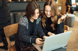 © Serhiy Hipskyy - Two girls, friends Drink Hot Coffee While Work In Cafe On Laptop. Portrait Of Stylish Smiling Girls In Winter Clothes Drinking Hot Coffee And Work At Laptop. Female Winter Style. - Image