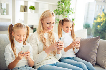 Sticker - Portrait of nice adorable cute attractive lovely lovable winsome charming people mom girls sitting on divan using device in light white interior room indoors