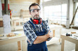 © Seventyfour - Serious confident handsome middle-aged carpenter in protective goggles standing in modern workshop and crossing arms on chest while looking at camera