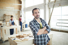 Content Confident Handsome Middle-aged Workman In Checkered Shirt Leaning On Table With Tools And Looking At Camera In Carpentry Shop