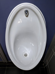 A shiny white porcelain urinal with purple medium density fibre board (MDF) fascia and stall separators in the gentlemen's toilets at an events venue 