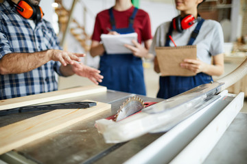 Wall Mural - Close-up of unrecognizable male carpenter gesturing hands while showing circular saw table to students during carpentry class at factory