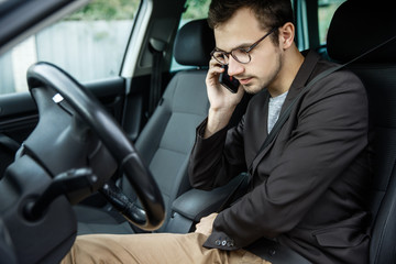 Wall Mural - Young guy clips on his belt while talking on the phone. He is sitting at his car. Road safety concept.