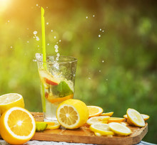 Fruit orange lemonade in a glass with splashes flying around on a natural background in the garden.