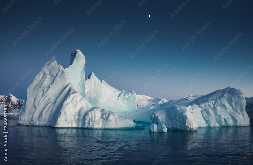 Close-up iceberg next to the Antarctica shoreline. The huge ice covered mountain with the basin. The glacier floating among the frozen polar ocean water. Breathtaking North pole landscape. - obrazy, fototapety, plakaty 