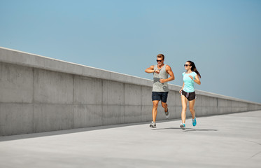 Poster - fitness, sport and lifestyle concept - happy couple in sports clothes and sunglasses running outdoors