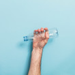 © ink drop - Hand holding empty plastic bottle recycling against a blue background