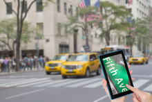 Female Finger Touching Tablet With Sign Fifth Avenue In The Touchscreen. Intentionally Blurred Image Of A Fifth Avenue (NYC) Is In The Background. All Potential Trademarks Are Removed.
