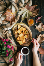 From Above Hands Of Anonymous Woman Holding Cup Of Hot Tea And Spreading Fresh Honey On Crunchy Croutons Near Autumn Leaves And Flowers On Lumber Tabletop