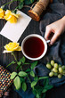 © ADDICTIVE STOCK - From above hand of anonymous female holding cup of aromatic tea near elegant yellow roses and empty note over wooden tabletop