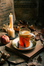 Cup Of Fresh Tea With Lemon Placed Near Ripe Apple And Flaming Candles Amidst Autumn Leaves