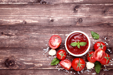 Ketchup in bowl with basil leafs and salt on brown wooden table