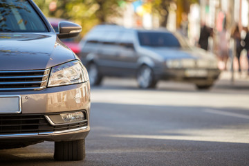 Wall Mural - Front view detail of gray shiny empty car parked on blurred green trees bokeh background on bright sunny day. Transportation and parking concept.