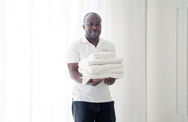 Portrait of african man a smiling hotel maid holding fresh clean folded towels for the room. Chambermaid man holding clean towels in hotel room