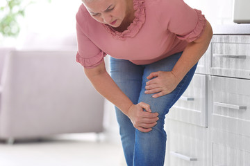 Wall Mural - Senior woman suffering from knee pain in kitchen